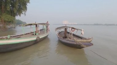 Bir nehir kıyısındaki bir rıhtımda halatla bağlanmış eski bir ahşap tekne çapası arka planda açık gökyüzüne karşı..