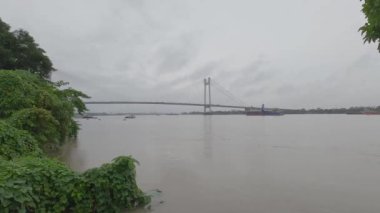 Vidyasagar Setu veya Hooghly Nehri üzerindeki İkinci Hooghly Köprüsü, yağmurlu bir günde önplanda çerçeve ağacı olan bulutlu bir gökyüzüne karşı. Kolkata Batı Bengal, Hindistan