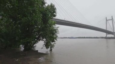 Vidyasagar Setu veya Hooghly Nehri üzerindeki İkinci Hooghly Köprüsü, yağmurlu bir günde önplanda çerçeve ağacı olan bulutlu bir gökyüzüne karşı. Kolkata Batı Bengal, Hindistan