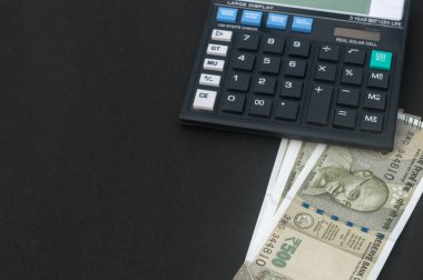 Masadaki hesap makinesinin altına yerleştirilmiş Hint Rupisi. Siyah arkaplanda izole.