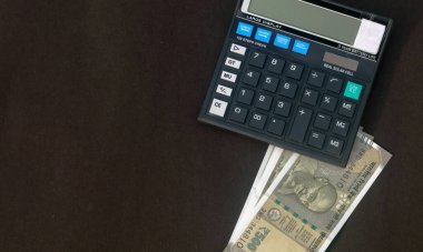 Masadaki hesap makinesinin altına yerleştirilmiş Hint Rupisi. Gri arkaplanda izole.