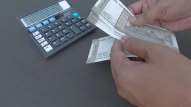 İnsan eli, hesap makinesine ve masaya yerleştirilmiş bir kaleme karşı 500 rupi Hindistan parası sayıyor. Yüksek açı. Kapatın. Bankacılık İşletme Finans Arkaplanı.