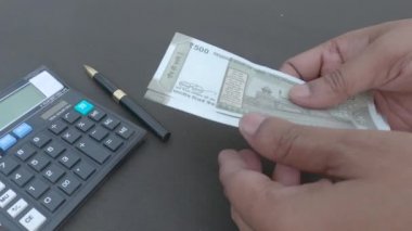 İnsan eli, hesap makinesine ve masaya yerleştirilmiş bir kaleme karşı 500 rupi Hindistan parası sayıyor. Yüksek açı. Kapatın. Bankacılık İşletme Finans Arkaplanı.