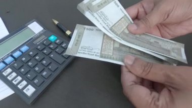 İnsan eli, hesap makinesine ve masaya yerleştirilmiş bir kaleme karşı 500 rupi Hindistan parası sayıyor. Yüksek açı. Kapatın. Bankacılık İşletme Finans Arkaplanı.