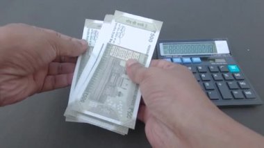 İnsan eli, hesap makinesine ve masaya yerleştirilmiş bir kaleme karşı 500 rupi Hindistan parası sayıyor. Yüksek açı. Kapatın. Bankacılık İşletme Finans Arkaplanı.