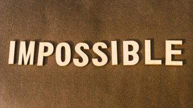 The word Impossible written with Brown Wooden Alphabet stamp on Vintage background.