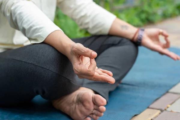 Close up woman mudra hand gesture doing yoga relaxing in lotus position sitting on mat. outdoors. Practicing meditation in nature. Background Photo.