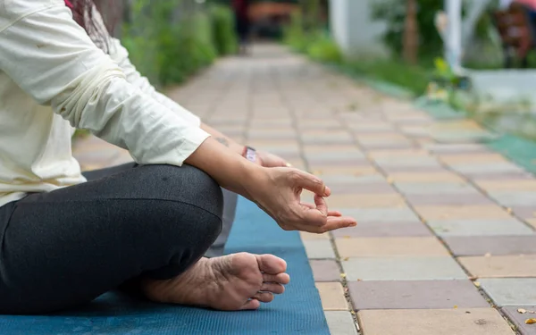 Close up woman mudra hand gesture doing yoga relaxing in lotus position sitting on mat. outdoors. Practicing meditation in nature. Background Photo.