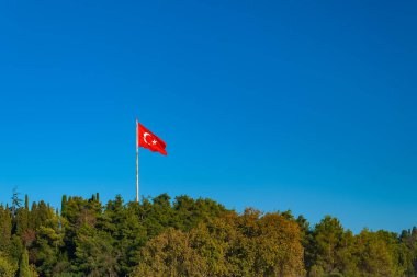 Türk bayrağı. Akşamları mavi gökyüzüne karşı bir dağ ormanının üzerinde Türk bayrağı. Turist konumu.