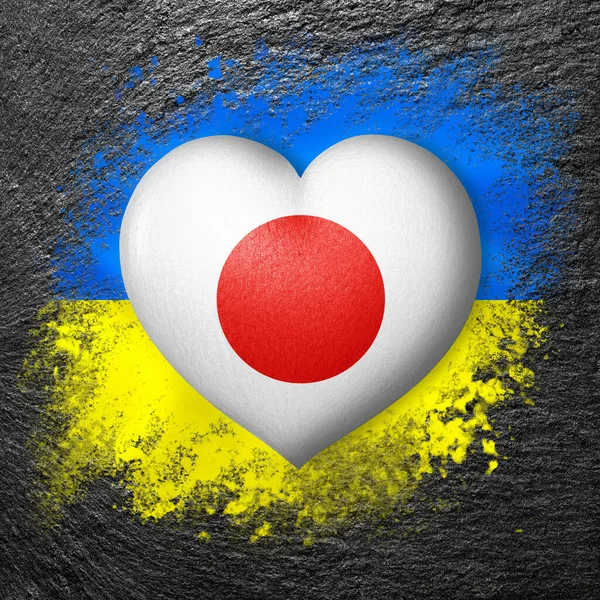 Flags of Ukraine and Japan. Flag heart on the background of the flag of Ukraine painted on a stone. The concept of protection and solidarity. Military and humanitarian assistance.