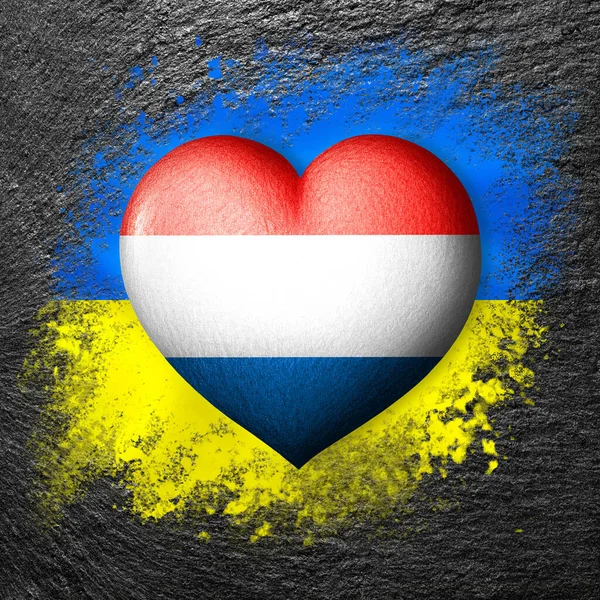 Flags of Ukraine and Netherlands.Flag heart on the background of the flag of Ukraine painted on a stone. The concept of protection and solidarity. Military and humanitarian assistance.