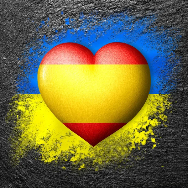 Flags of Ukraine and Spain. Flag heart on the background of the flag of Ukraine painted on a stone. The concept of protection and solidarity. Military and humanitarian assistance.