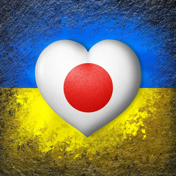 Flags of Ukraine and Japan. Flag heart on the background of the Ukrainian flag painted on a stone. The concept of protection and solidarity. Military and humanitarian assistance.