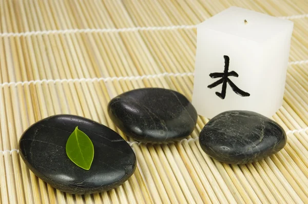 Black zen pebbles, green leaf and japanese candle — Stock Photo, Image