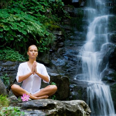 Young woman doing yoga near waterfall