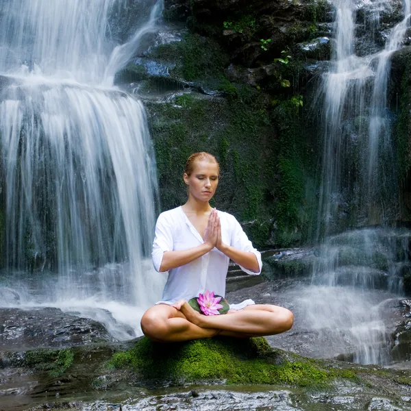 Şelalenin yakınında yoga yaparken genç bir kadın — Stok fotoğraf