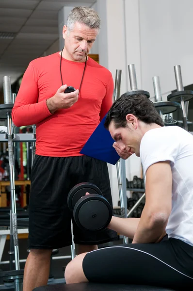 Junger Mann mit Trainer im Fitnessstudio — Stockfoto