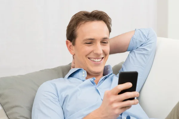 Мужчина лежит на диване с сотовым телефоном — стоковое фото