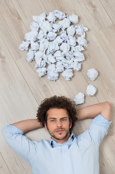 Junger Mann liegt mit zerknitterten Papieren auf dem Boden — Stockfoto