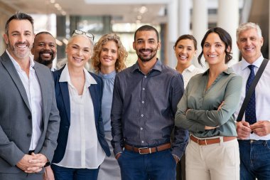 Modern ofiste kameraya bakan başarılı iş adamlarının portresi. Mutlu iş adamlarının portresi ve takım olarak ayakta duran tatmin olmuş iş kadınları. Çok ırklı bir grup insan gülümseyip kameraya bakıyor..