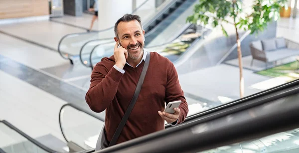 사업가 공항에서 이어폰을 사용하는 에스컬레이터를 올라가 스마트폰 통화를 있습니다 현대적 — 스톡 사진