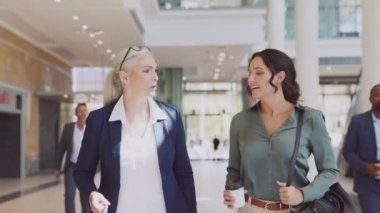 Modern ofiste yürüyen ve konuşan iki iş kadını. İki başarılı kadın yönetici ofis binasına girerken iş hakkında konuşuyor. İşe giderken asistanıyla konuşan başarılı bir iş kadını..