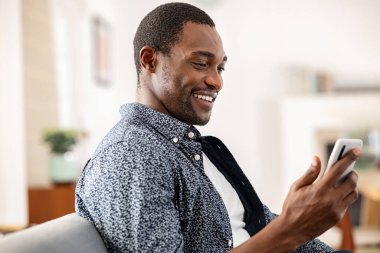 Mutlu orta yaşlı bir adam akıllı telefon kullanırken koltukta dinleniyor. Yakışıklı siyahi adam cep telefonundan mesaj okuyor. Orta yaşlı gülümseyen Afrikalı adam evde dinleniyor ve cep telefonuyla video görüşmesi yapıyor..