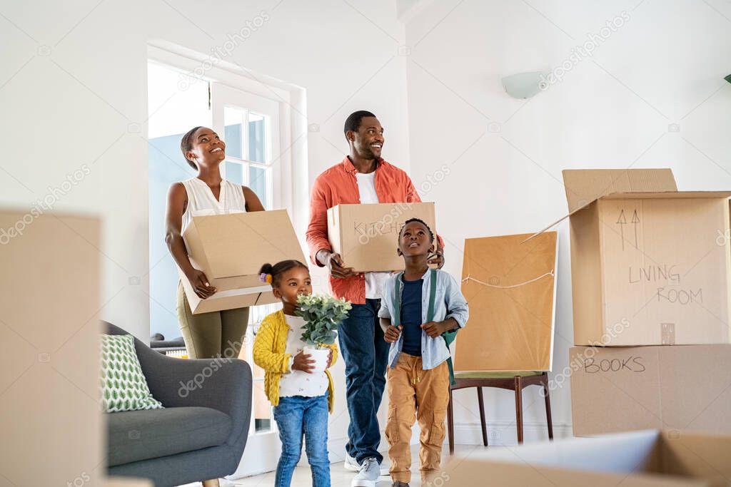 Beautiful african american family with two children carrying boxes in a new home. Cheerful mature mother and mid adult father holding boxes while entering new home with son and daughter. Happy son and daughter helping parents relocating in new house 