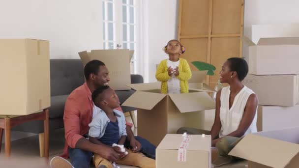 快乐的黑人小女孩站在一个大盒子里玩聚苯乙烯泡沫片 快乐的非洲裔美国家庭享受着新的家园 有儿子和有趣女儿的成熟父母在搬家时很开心 — 图库视频影像