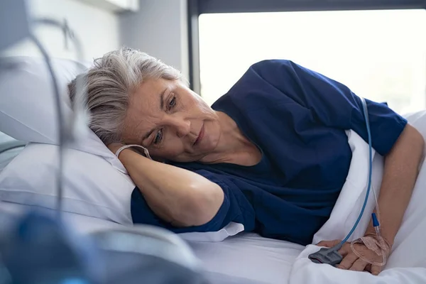 病院のベッドの上に横になった悲しい先輩女性が見下ろしている 4滴を手に診療所でゴニーに寝そべっている老患者をうつ状態にした 末期疾患の老女が病院病棟で休んでいる — ストック写真