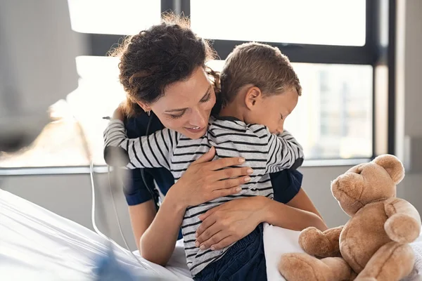 入院中の病気の少年を抱きしめる幸せな看護師 若い医療従事者はクリニックで動揺した子供を受け入れる 素敵な医師が私立クリニックでかわいい子供の世話をする 感謝と医療の概念 — ストック写真