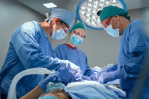 Team of experienced surgeons with surgical mask working together in a operation room. Medical staff of professional surgeons wearing protection and surgical cap while performing surgery on a patient in the operation theater. Group of surgeons at work