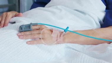 Eline serum fizyolojik solüsyon tüpü damlatarak yaşlı kadına yakın durun. Olgun bir hasta hastanede tedavi edilirken elinde serum damlatarak hastaneye kaldırıldı. Nabız oksimetresi eski hastada nabız ve oksijen seviyelerini ölçmek için kullanılır..