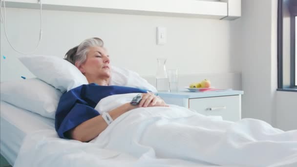 悲伤的老妇人躺在医院的病床上 望着别处 沮丧的老妇人躺在医院病房的白色被单上 凝视着窗外 陷入沉思 住院老年妇女卧床康复 — 图库视频影像