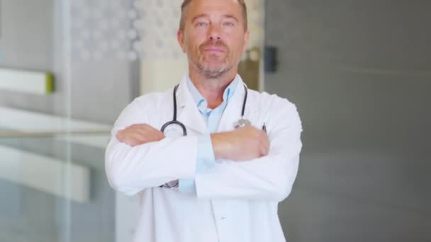 一个幸福而成熟的医生的画像 双臂交叉地站在医院的走廊上 穿着工作服和听诊器自信的男医生满意地看着相机 在私营诊所微笑自信的全科医生 — 图库视频影像