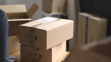 Teslimat paketinde barkodu tarayan genç bir kadının elleri. Depoya teslim edilmeden önce karton paketlerin barkodlarını tarayın. Fabrika deposunda çalışan bir kadın bluetooth barkod tarayıcısıyla kutulardaki etiketleri okuyup tarıyor..