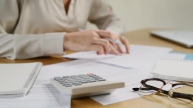Aylık giderlerini hesaplamak için hesap makinesi kullanan bir kadın. Finansal verilerle çalışan ve ofiste hesap makinesi kullanan iş kadınlarını kapatın. Ev finansmanı ve yıllık vergileri hesaplayan ellerin ölümü.