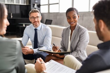 Group of business people sitting together and having discussion during a work meeting. Diverse businessmen and business women working in teamwork discussing project strategy. Mature african businesswoman writing notes during a brainstorming with coll