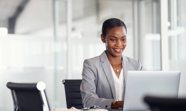 Happy black business woman working on laptop at modern office. Focused mature businesswoman checking email in meeting room with copy space. African american manager typing on a keyboard in her office.