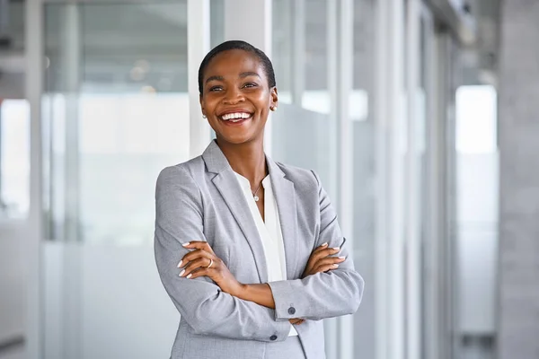Confident and successful business woman in suit looking away and smiling. Portrait of mature black businesswoman standing in office with copy space. African american business woman in formal clothing standing in modern office: vision and future busin