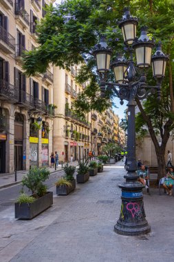 Barselona, İspanya - 22 Eylül 2021: Tipik geleneksel şehir manzarasında antik sokak lambası. Dar balkonlu ve demir parmaklıklı evler. Yol kenarındaki ağaçlar gölge sağlar. Şehir görünümü