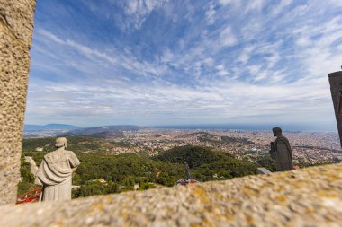 Barselona, İspanya - 23 Eylül 2021: Parc Tibidabo 'nun zirvesindeki İsa' nın Kutsal Kalbi Kilisesi 'nin çatısından bakın. Havadan şehir manzarası. Önplanda taş heykeller.