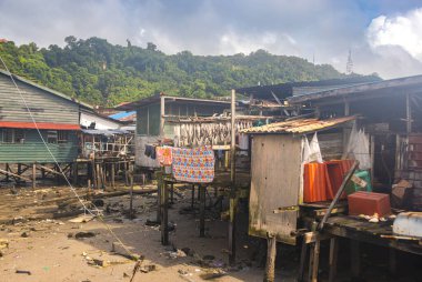 Sandakan, Malezya - 06 Ocak 2022: Sandakan, Borneo şehir merkezine yakın bir balıkçı köyü. Kıyıdaki sahil suyunda tahta bacaklı zavallı kulübeler. Plastik çöpler okyanusu ve sahili kirletiyor..