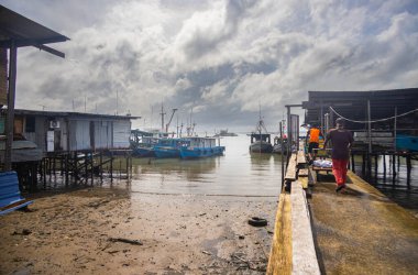 Sandakan, Malezya - 06 Ocak 2022: Sandakan, Borneo şehir merkezine yakın bir balıkçı köyü. Kıyıdaki sahil suyunda tahta bacaklı zavallı kulübeler. Plastik çöpler okyanusu ve sahili kirletiyor..