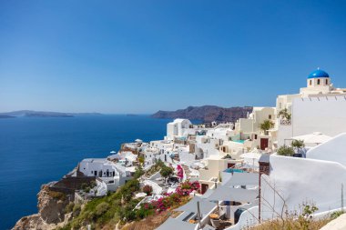 Santorini, Greece - August 7, 2021: View over the roofs of the typical houses of Santorini, island in the cyclades archipelago in the Aegean Sea. White Houses under blue sky. Village high on the cliff