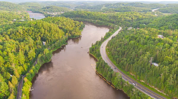 Wakefield, Kanada yakınlarındaki Gatineau Nehri 'nin havadan görünüşü. Nehir suyuna yansıyan bulutlar, nehir boyunca sürüklenen arabalı bir cadde. Yeşil yemyeşil Kanada orman manzarası