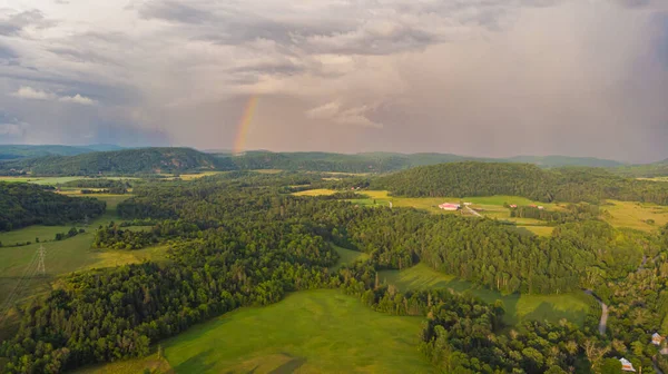 Kanada manzarasının uçsuz bucaksız ufkunda gökkuşağı. Yeşil çayır, tepedeki yemyeşil orman. Mavi gökyüzüne karşı yağmur bulutları, kara bulutların arasında güneş ışınları parlıyor. Ufukta gökkuşağı beliriyor