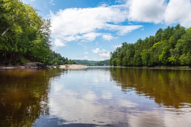 Wakefield, Quebec, Kanada yakınlarındaki Gatineau nehrinde. Nehir kıyısı seni soğuk suda yüzmeye davet ediyor. Boş günlerde dinlenmek için ideal bir yer. Etrafı sık ormanlarla çevrili. Beyaz bulutlar