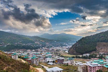 Thimphu, Bhutan - October 26, 2021: Aerial view cityscape of Bhutan capitol city. Top view with dramatic cloudy sky over the town. Largest city in Bhutan in a mountain valley. Houses with green roof