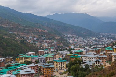 Thimphu, Bhutan - October 26, 2021: Aerial view cityscape of Bhutan capitol city. Top view with dramatic cloudy sky over the town. Largest city in Bhutan in a mountain valley. Houses with green roof